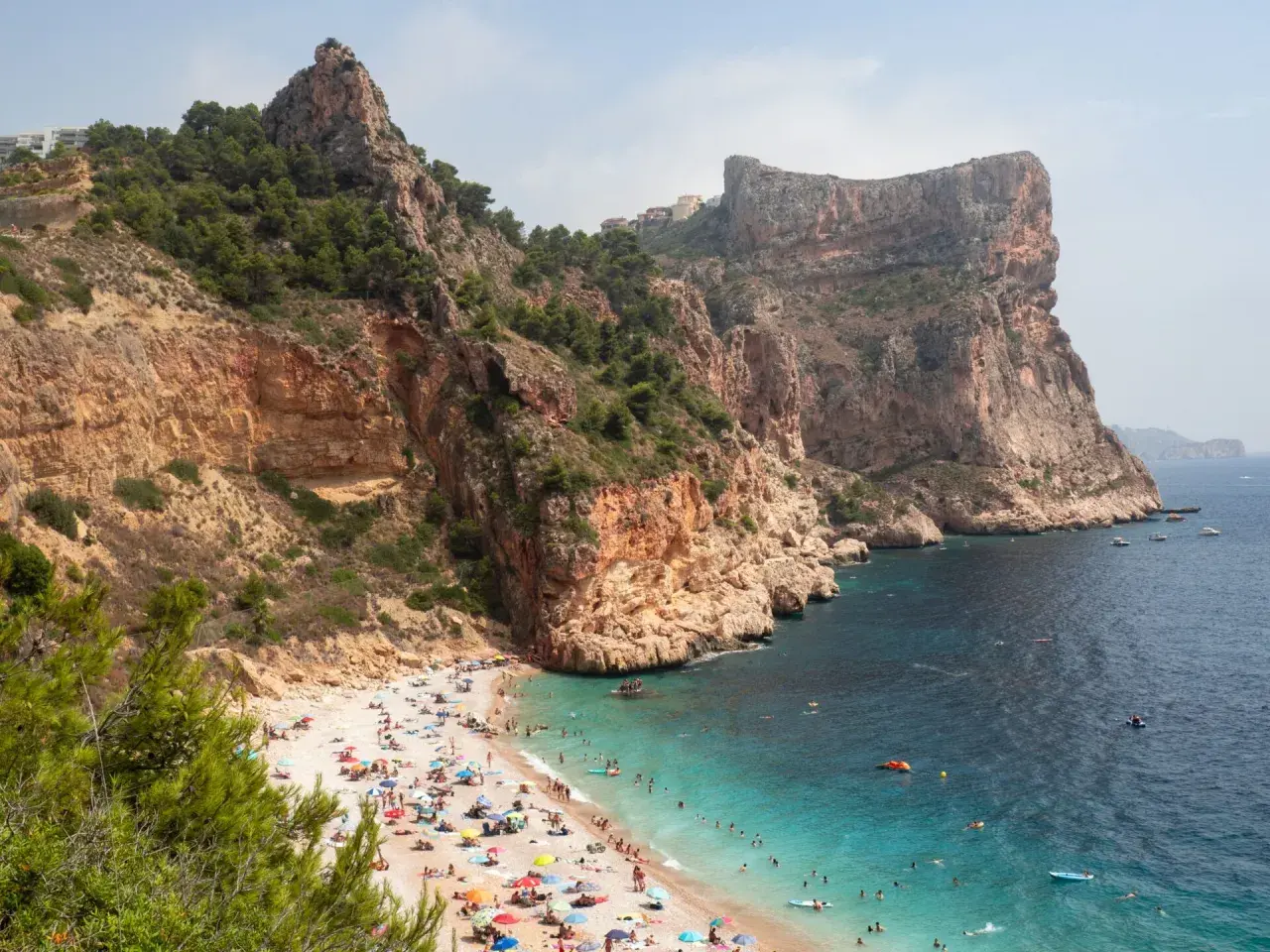 Una cala rocosa con aguas turquesas, gente disfrutando del sol y el mar. Un paraíso entre las mejores playas de la Costa Blanca.