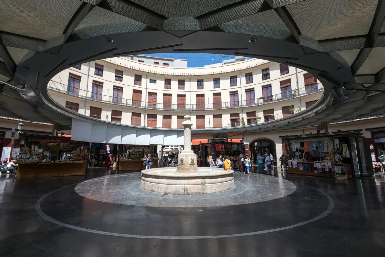 Fuente central en la plaza redonda valencia, rodeada de edificios curvos y puestos de venta.