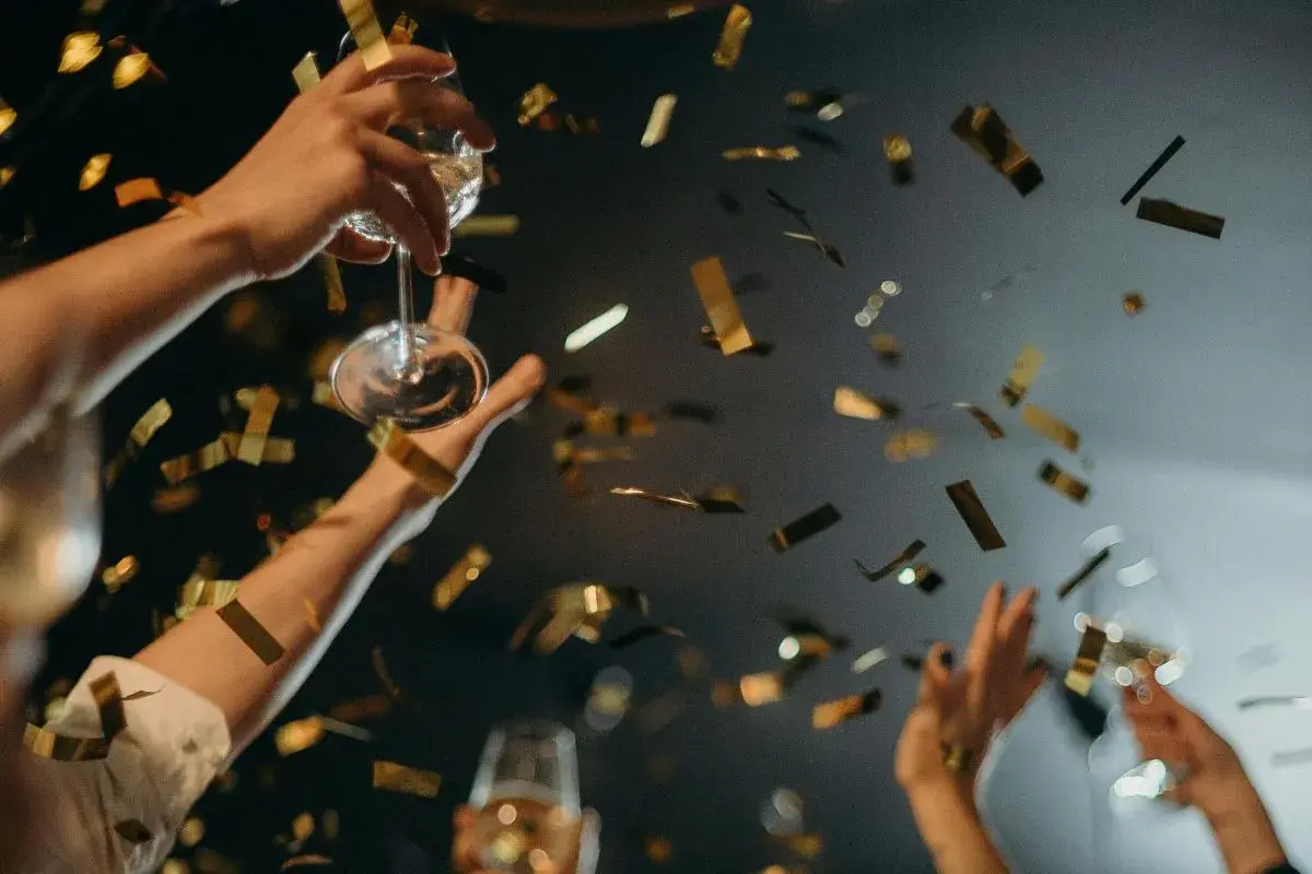 Manos brindando con copas y confeti dorado cayendo. ¡Una celebración perfecta para saber qué hacer en Nochevieja en Valencia!