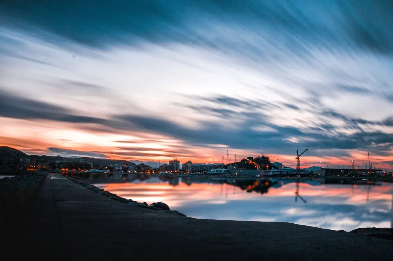 Atardecer en un puerto, con reflejos vibrantes en el agua. ¿Costa Blanca o Costa del Sol? La belleza es innegable.