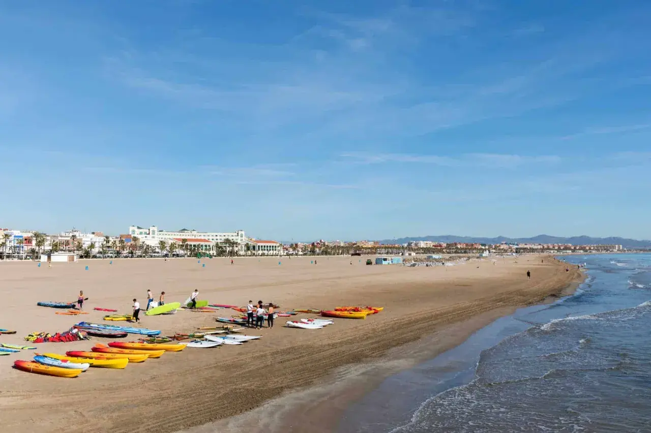 Gente prepara kayaks y tablas en la playa Malvarrosa, lista para un día de sol y mar.