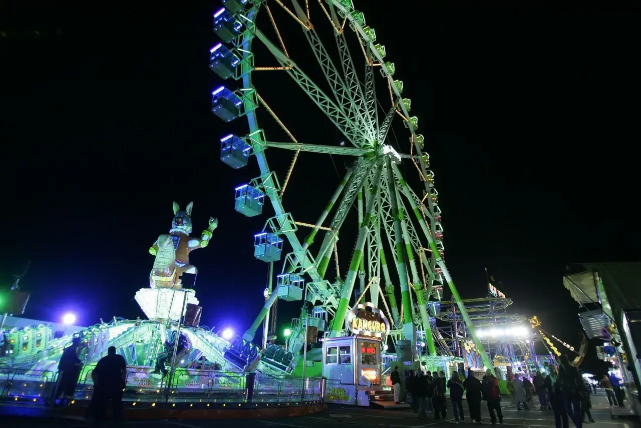 Noche de luces y diversión en la feria de Valencia. Atracciones como la noria y el Kanguro brillan con colores vibrantes.