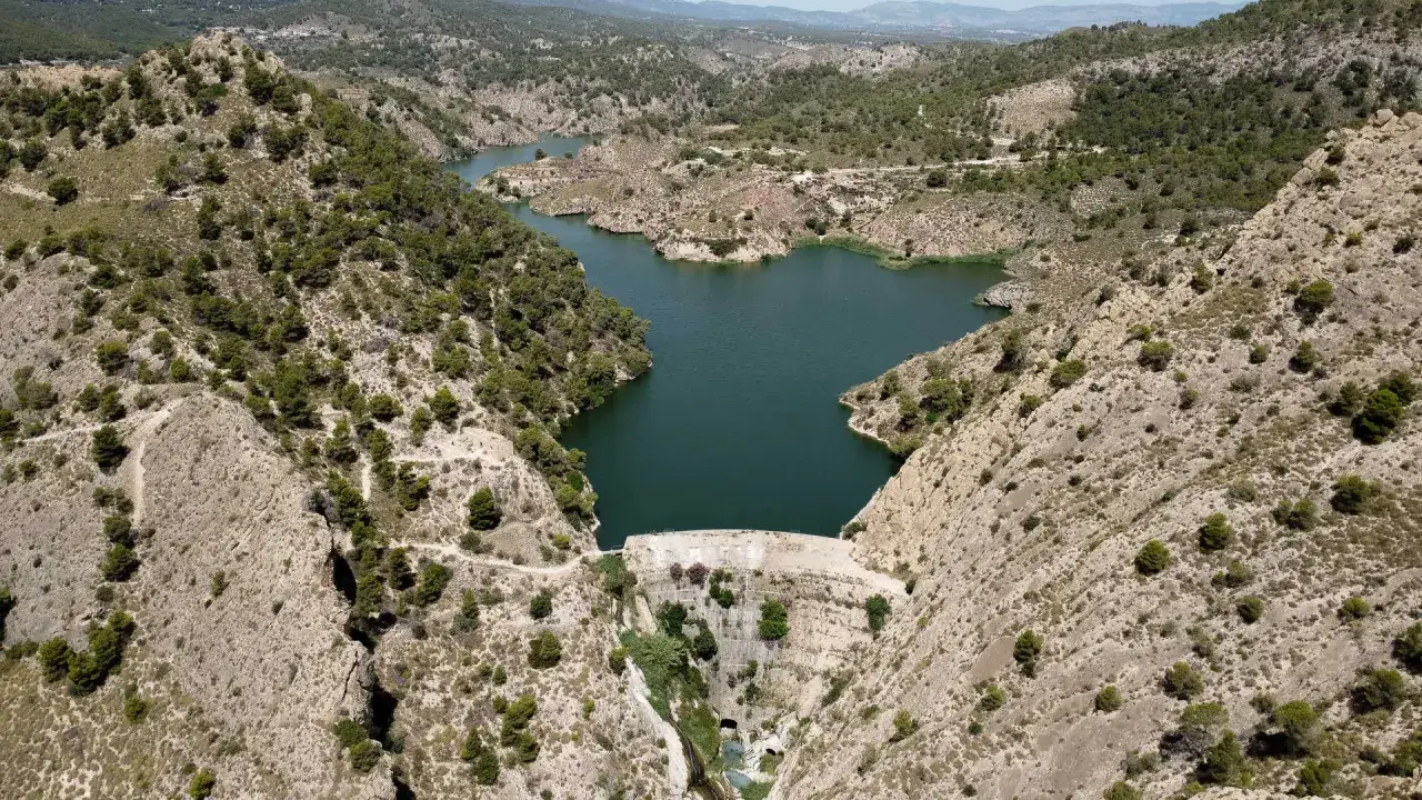 Vistas aéreas del pantano de Tibi, con su embalse de agua verde rodeado de colinas áridas y vegetación escasa.