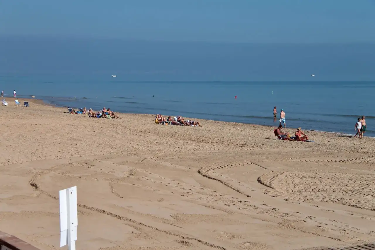 Gente relajándose en la playa la roqueta, con el mar azul y tranquilo de fondo.