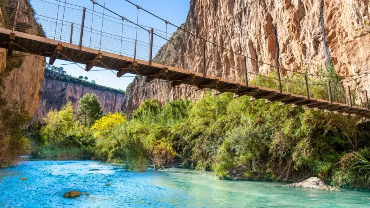 Puente colgante sobre río turquesa, ideal para excursiones cerca de Valencia. Naturaleza exuberante y cañones imponentes.