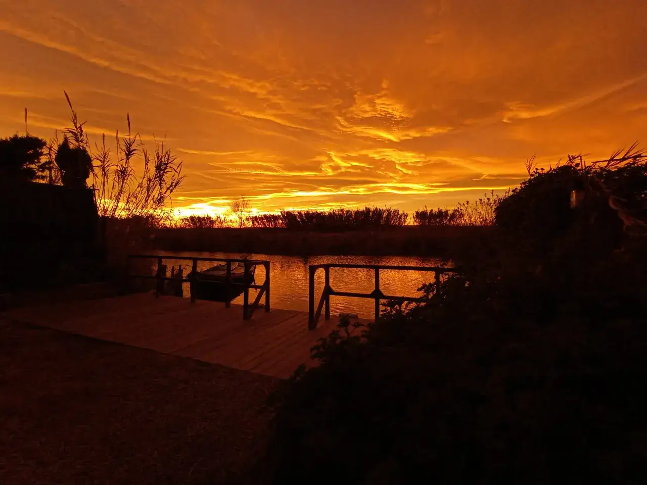 Atardecer anaranjado sobre la albufera Valencia, con un embarcadero de madera y una barca.