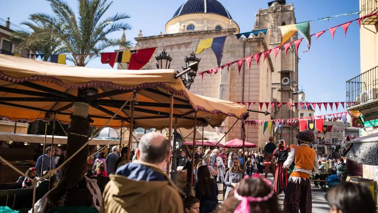 Gente disfrutando del orihuela mercado medieval, con puestos, banderas y edificios históricos.