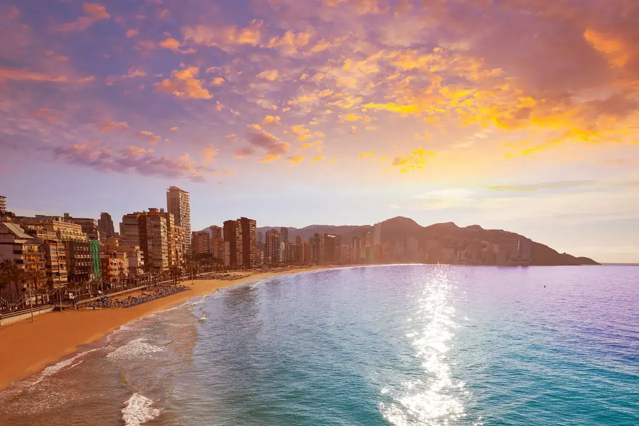 Atardecer en la Costa Blanca, con su playa dorada y edificios altos. Un contraste vibrante con la Costa del Sol.