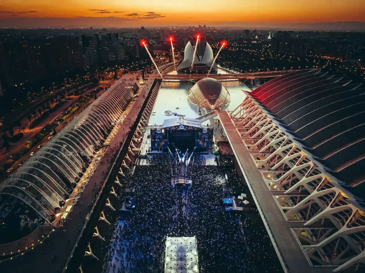 Gran multitud en el concierto de Quevedo, con fuegos artificiales iluminando el cielo al atardecer sobre la Ciudad de las Artes y las Ciencias.
