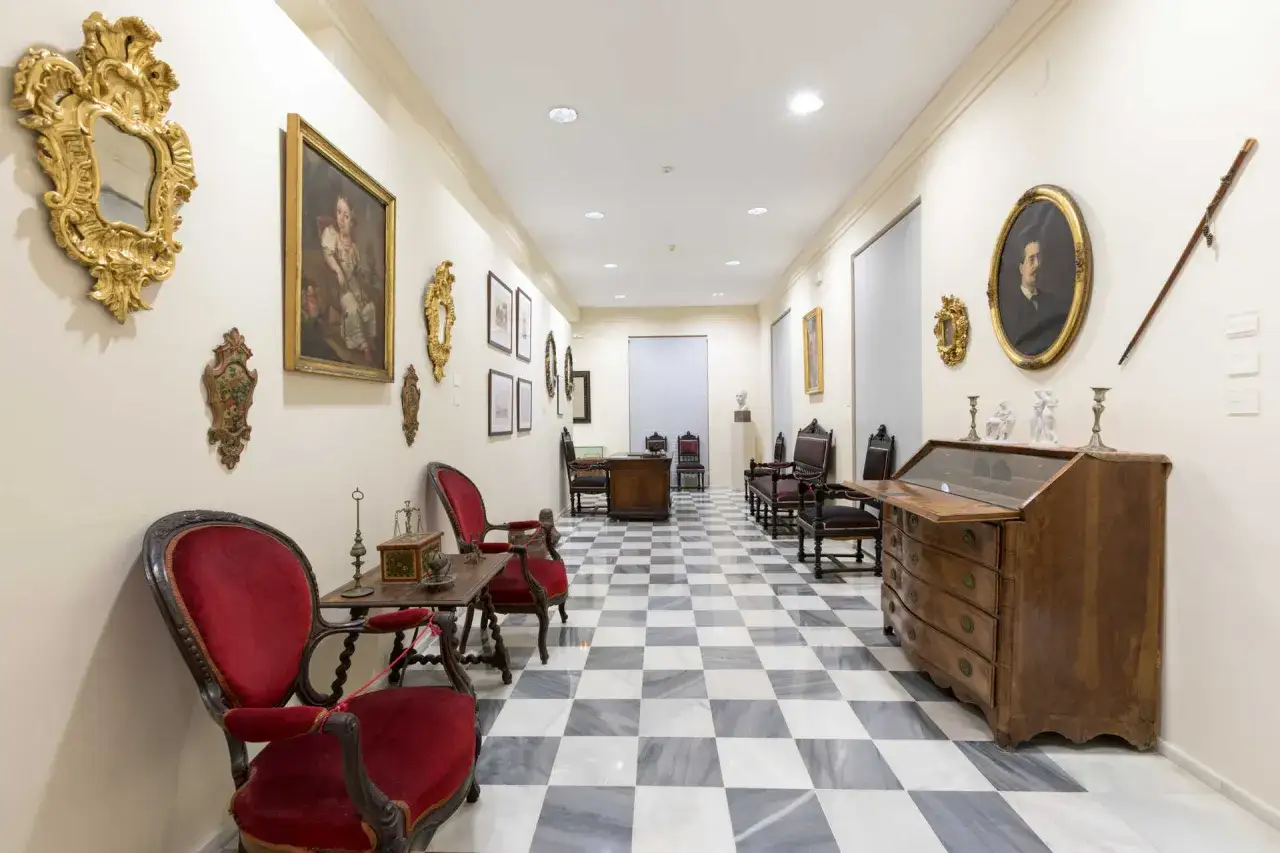 Pasillo de la casa museo Blasco Ibáñez con muebles antiguos, cuadros y un suelo de damero.