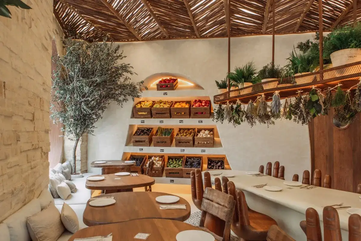 Interior de restaurantes valencia con estanterías de frutas y verduras frescas, árbol decorativo y mesas de madera.