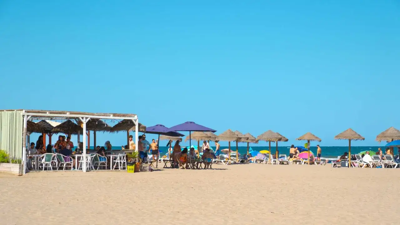 Gente disfrutando en la playa de la Patacona bajo sombrillas y en un chiringuito.