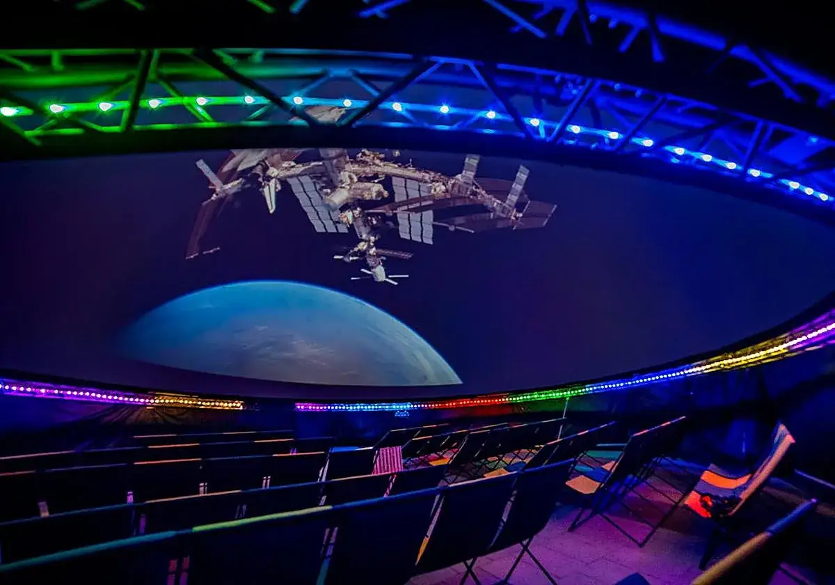 Asientos vacíos en el planetario Valencia, con la Estación Espacial Internacional y la Tierra proyectadas en la cúpula.