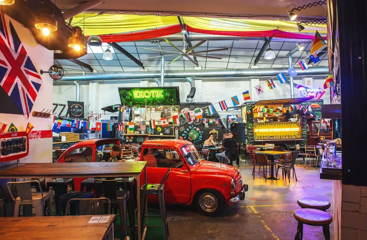 Un espacio vibrante con coches vintage y banderas internacionales, ideal para disfrutar de la oferta de restaurantes tem&aacute;ticos Valencia.