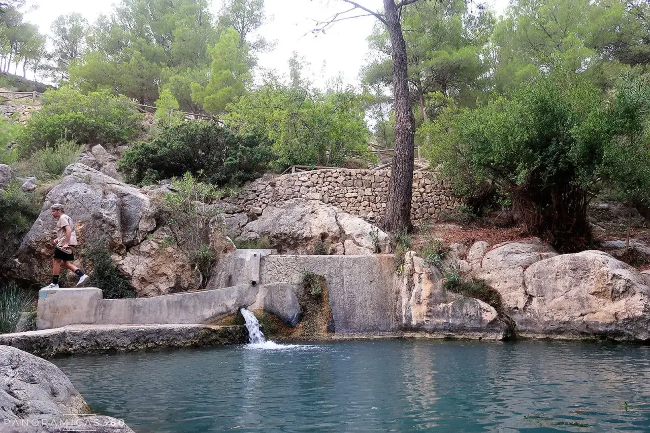 Un hombre camina junto a una cascada en un entorno natural, un lugar que parece un pequeño paraíso en Sella, Alicante.