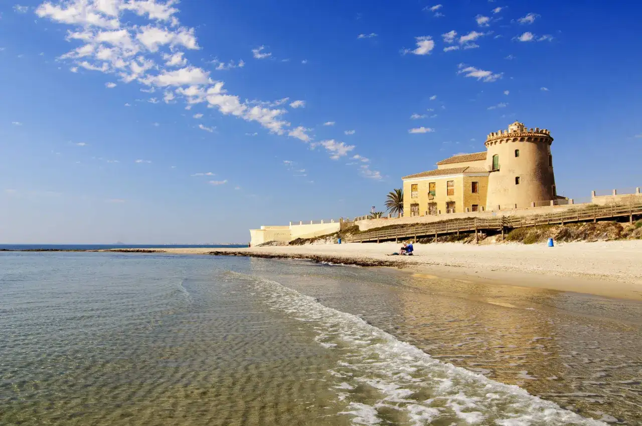 La playa del Conde, con su torre histórica y el mar azul bajo un cielo nublado, invita a la calma.