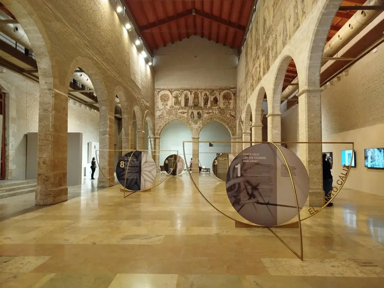 Interior del Almud&iacute;n de Valencia, con arcos de piedra, murales antiguos y una exposici&oacute;n circular sobre el Santo C&aacute;liz.