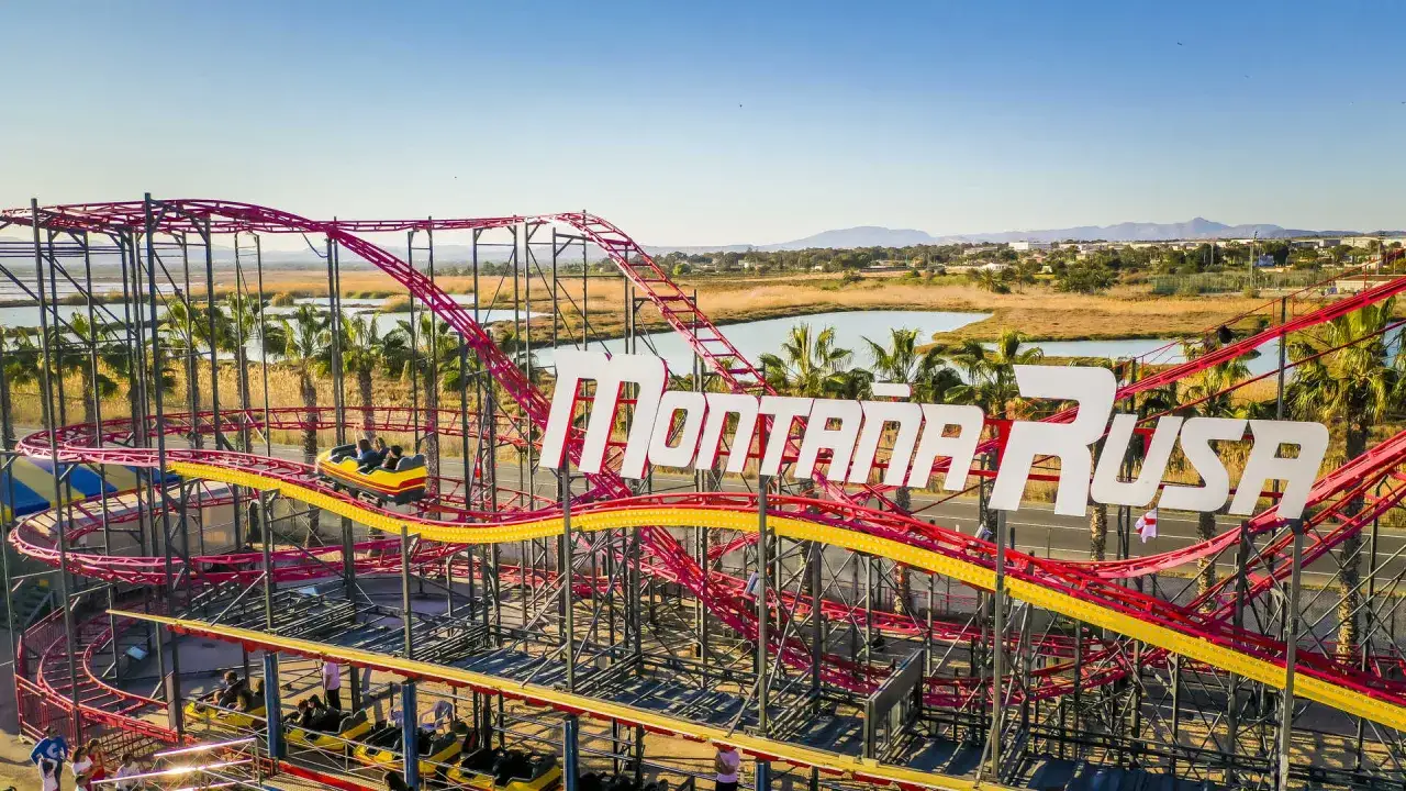 Montaña Rusa en Santa Pola Park, con un vagón en pleno recorrido y palmeras al fondo.
