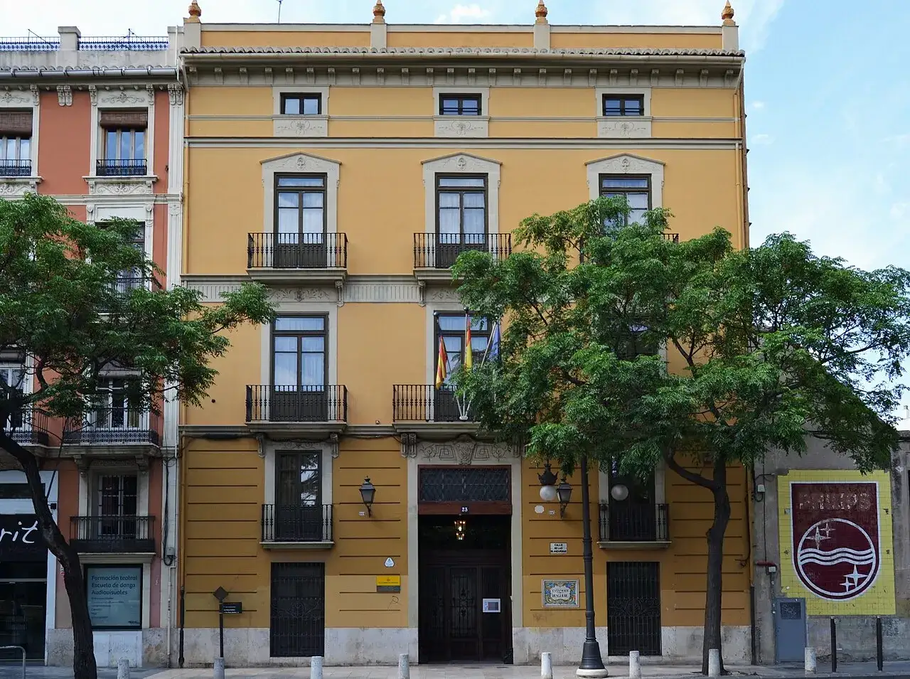 Fachada de la casa museo Benlliure, edificio amarillo con balcones y árboles frondosos delante.