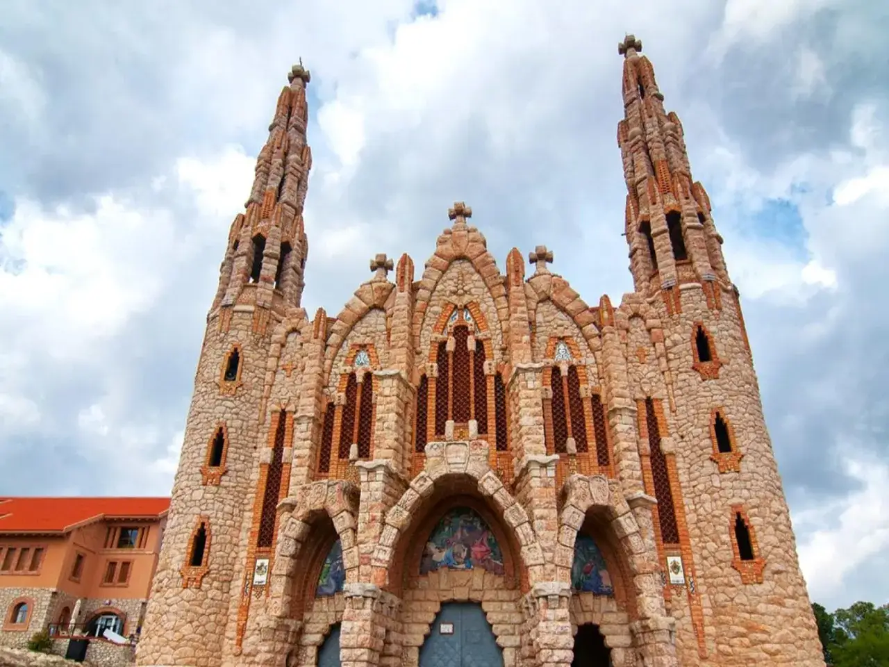 El Santuario de Novelda, con sus torres puntiagudas y su fachada de piedra, se alza majestuoso bajo un cielo nublado.
