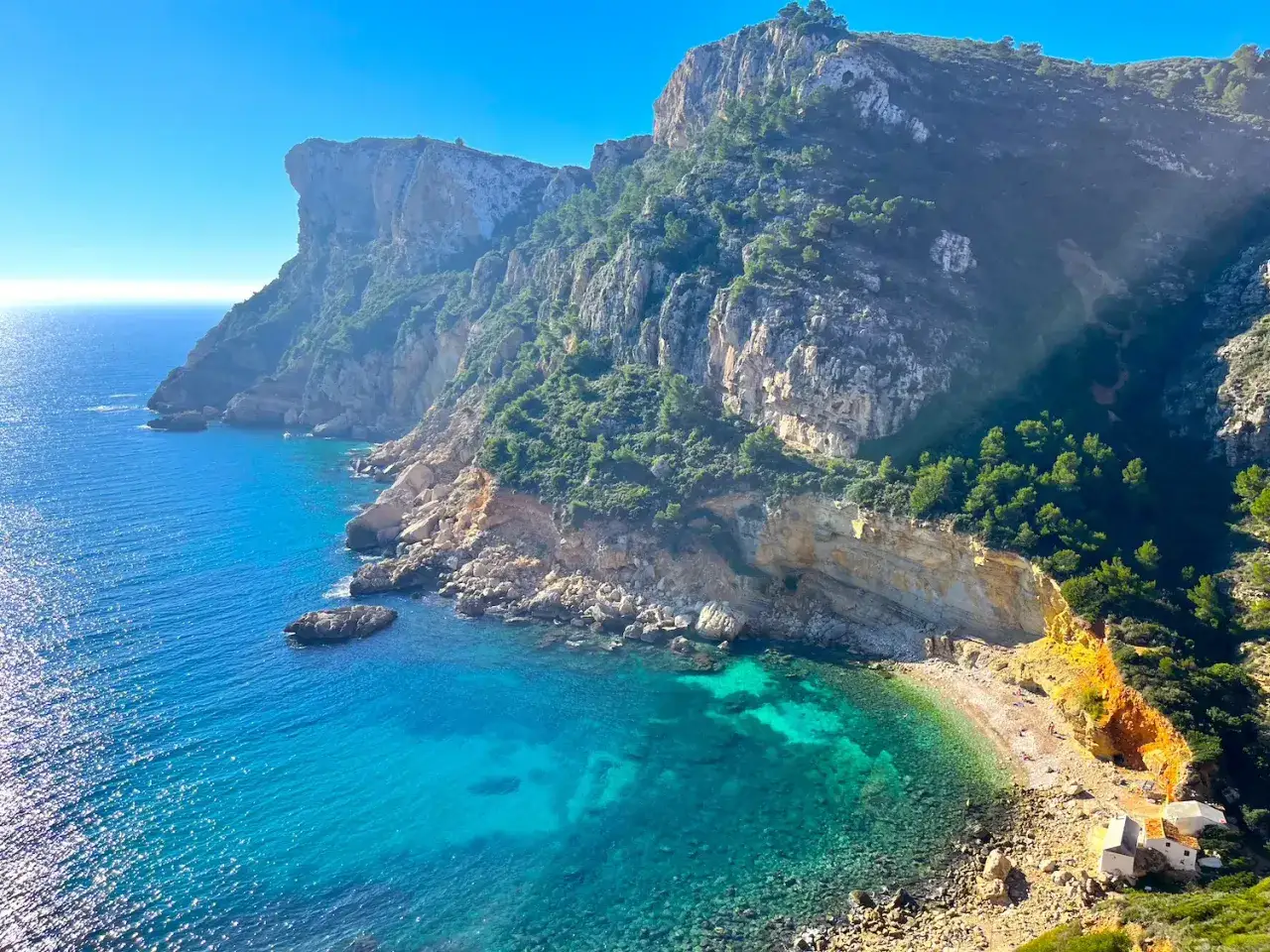 La cala Llebeig, una joya escondida entre acantilados, con aguas turquesas y casitas blancas.