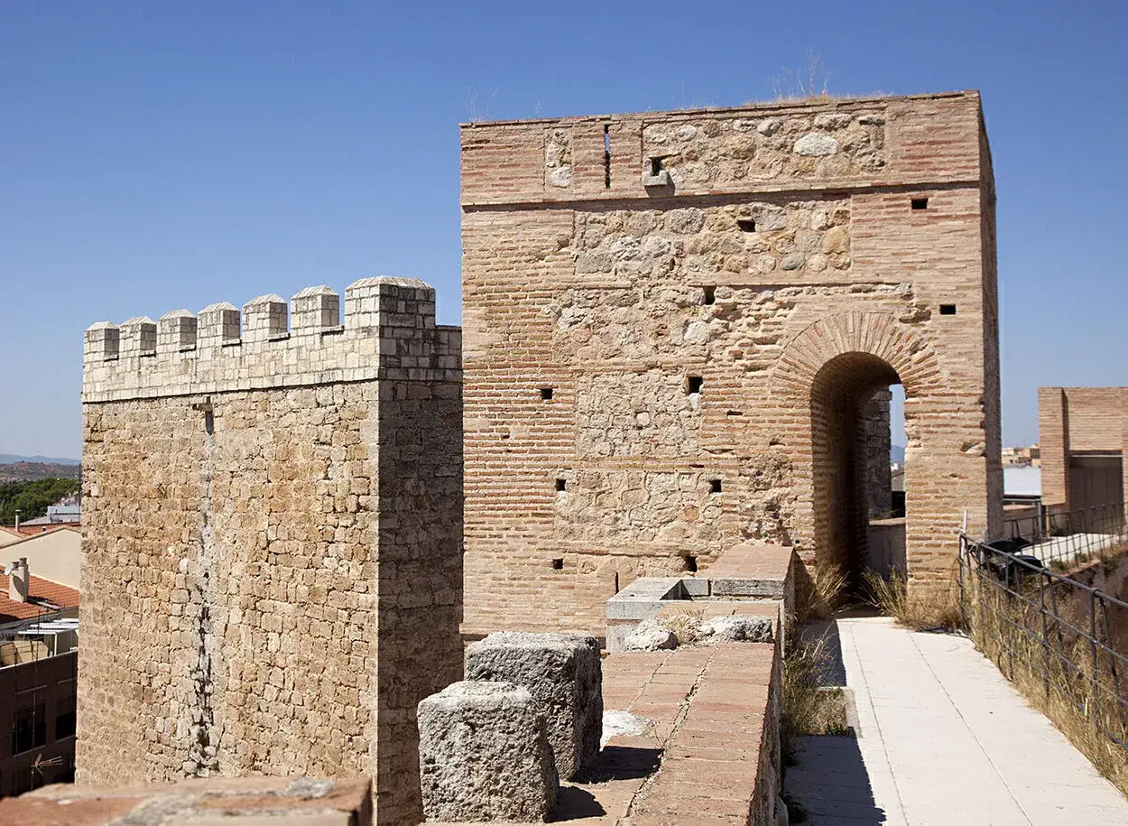 Antiguas murallas del castillo de Requena, con torres de piedra y ladrillo bajo un cielo azul.