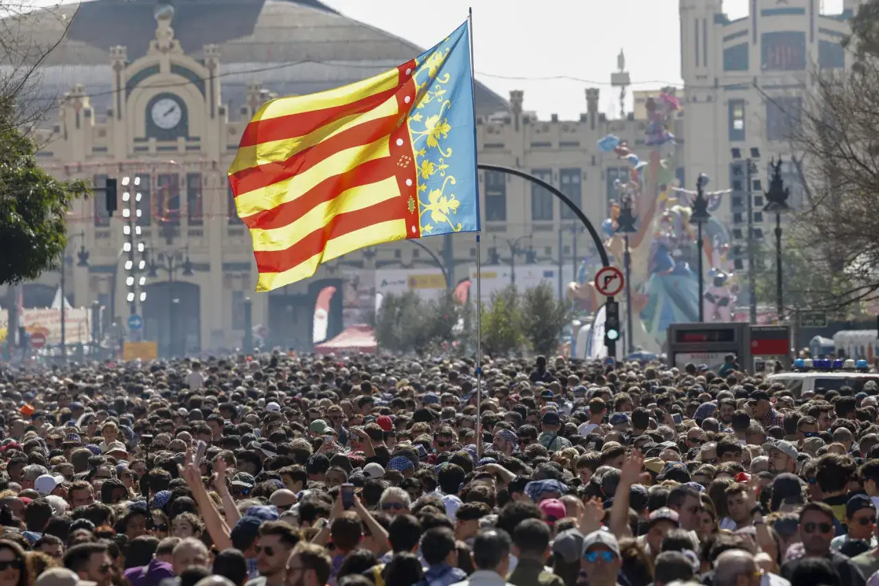 Multitud expectante ante la mascletà hoy en Valencia. Bandera valenciana ondea sobre un mar de gente.