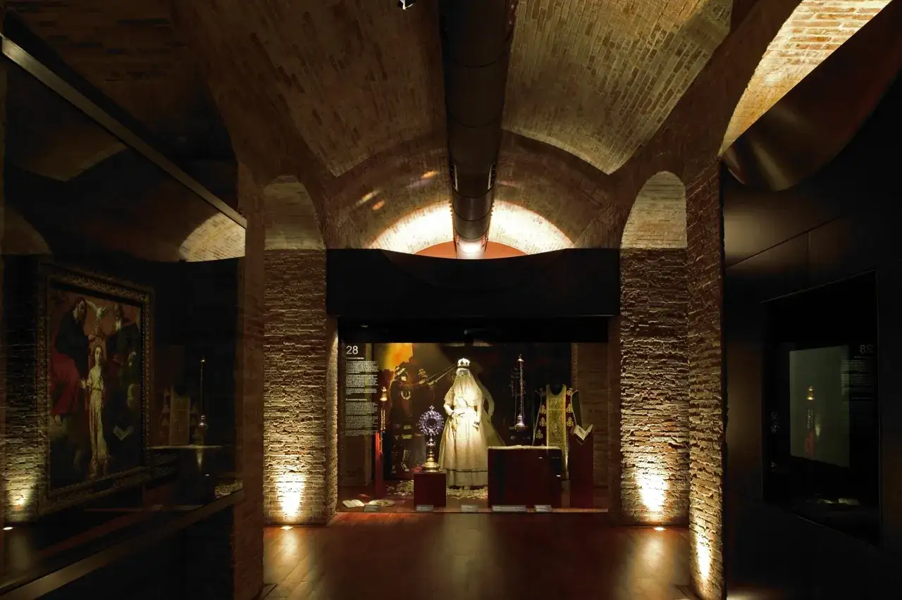 Exhibición en el museo de historia de Valencia: vestimentas religiosas, un cuadro y objetos litúrgicos en un espacio abovedado de ladrillo.