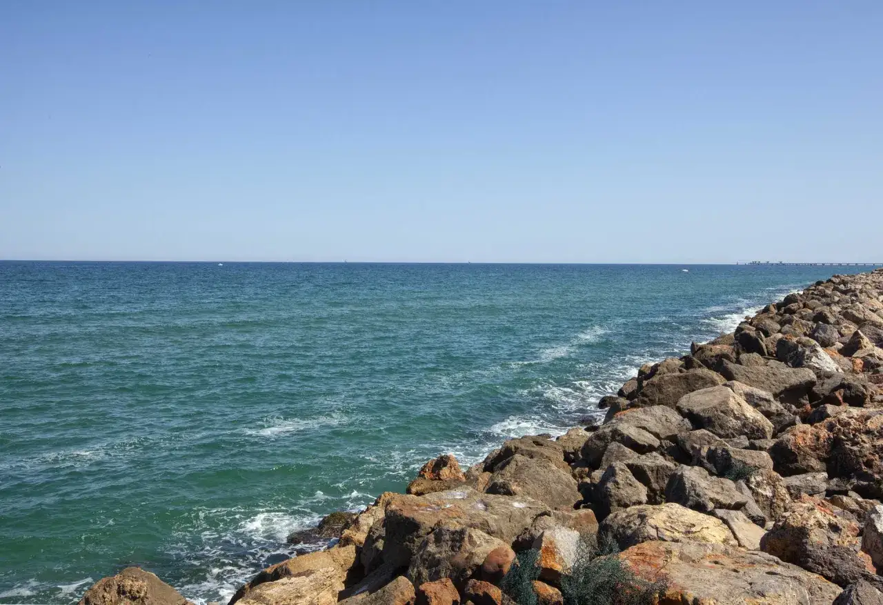 El mar turquesa baña las rocas de la playa Raco de la Mar. El cielo azul se funde con el horizonte.