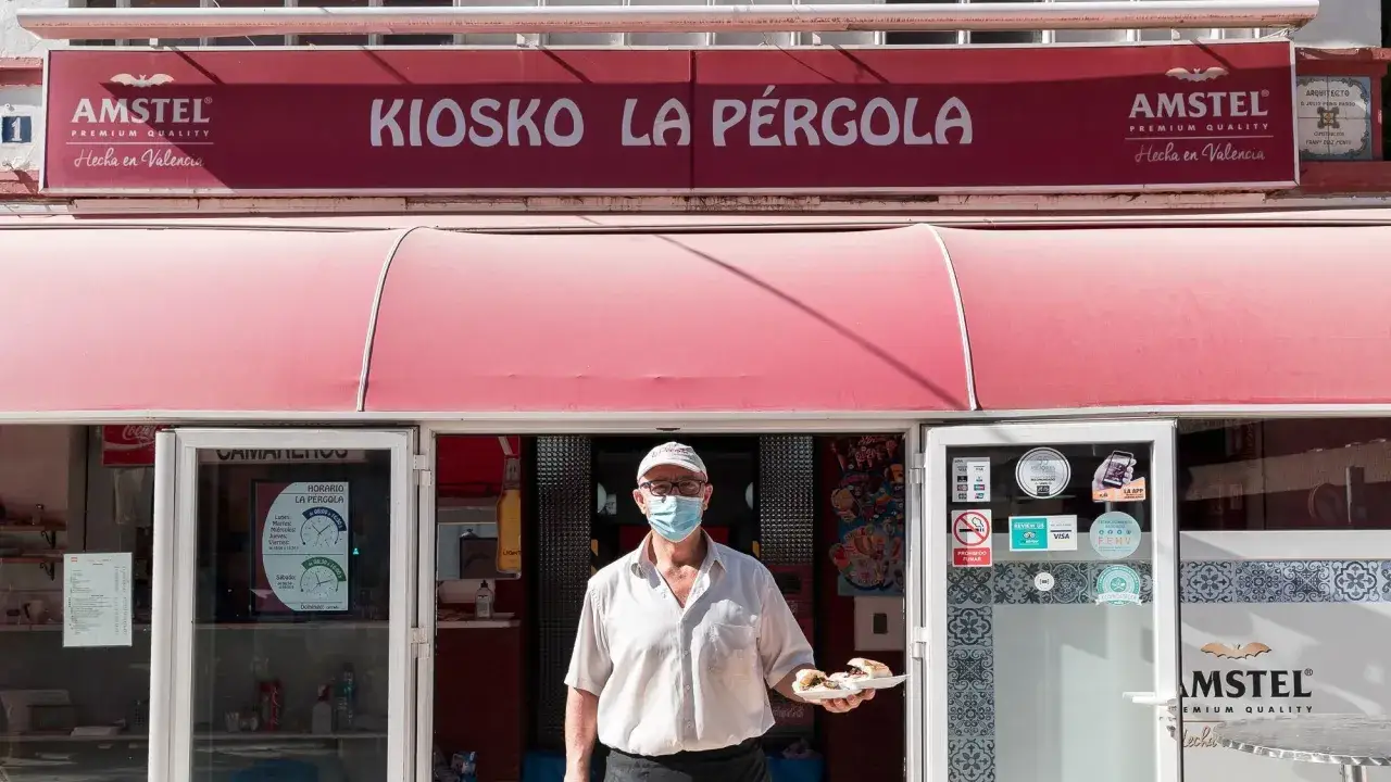 Hombre con mascarilla en la entrada de la pergola valencia, sosteniendo un plato con comida.