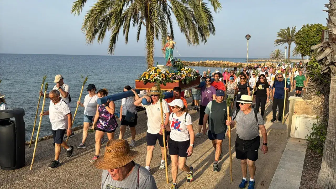 Procesión religiosa en la playa de la ermita Santa Pola. Gente camina con una imagen de la Virgen, portando palmas.