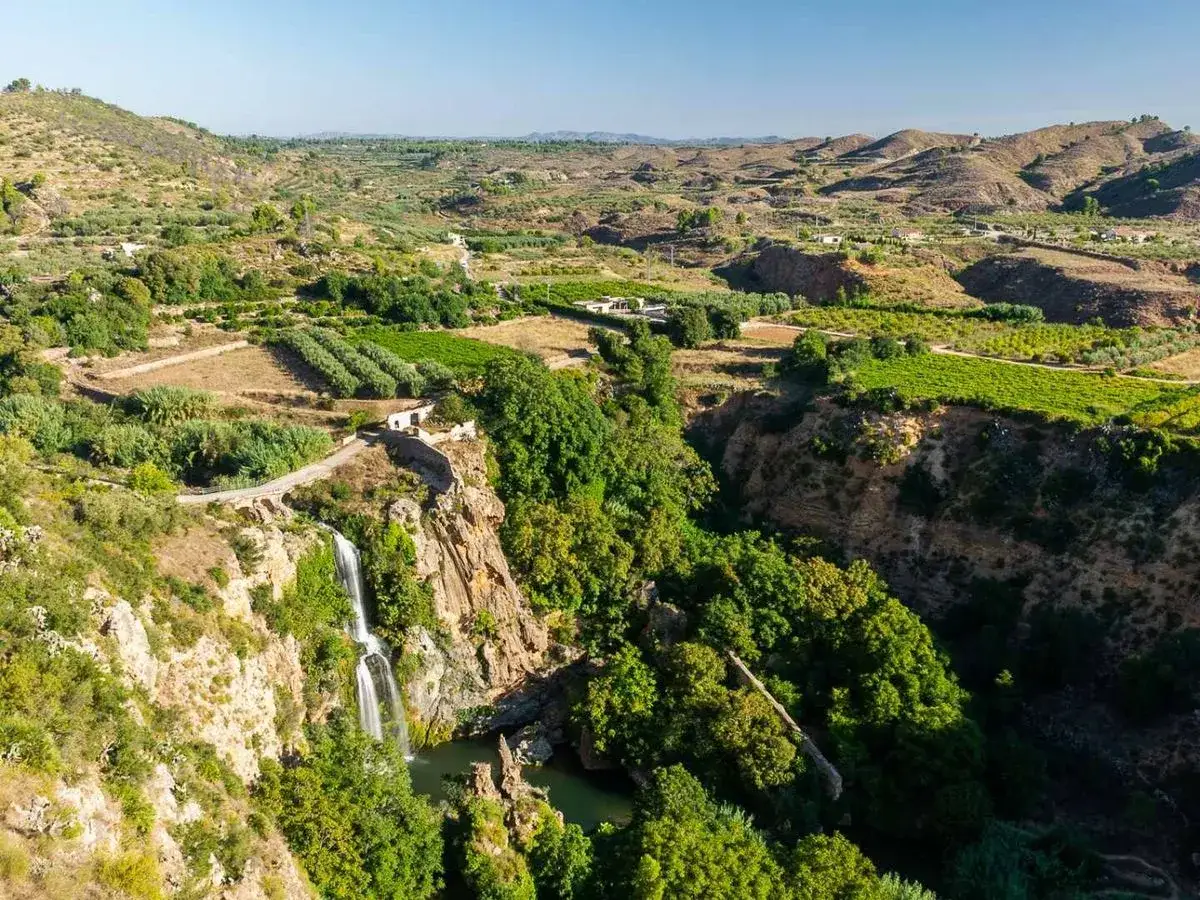 El Salto de Chella, una cascada que cae en un profundo cañón rodeado de vegetación exuberante y campos cultivados.