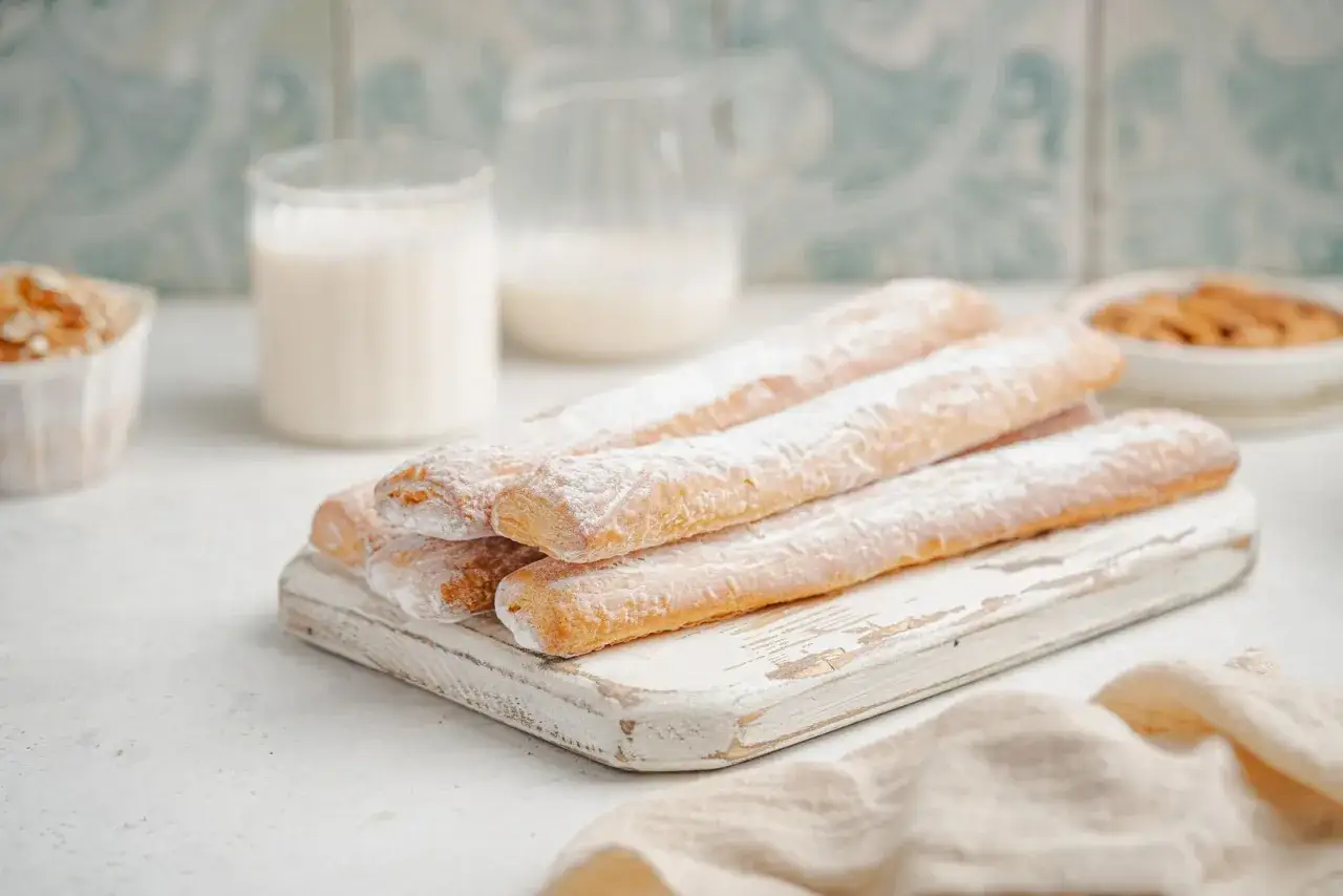 Dulces típicos de Valencia: palitos dorados espolvoreados con azúcar glas sobre tabla de madera.