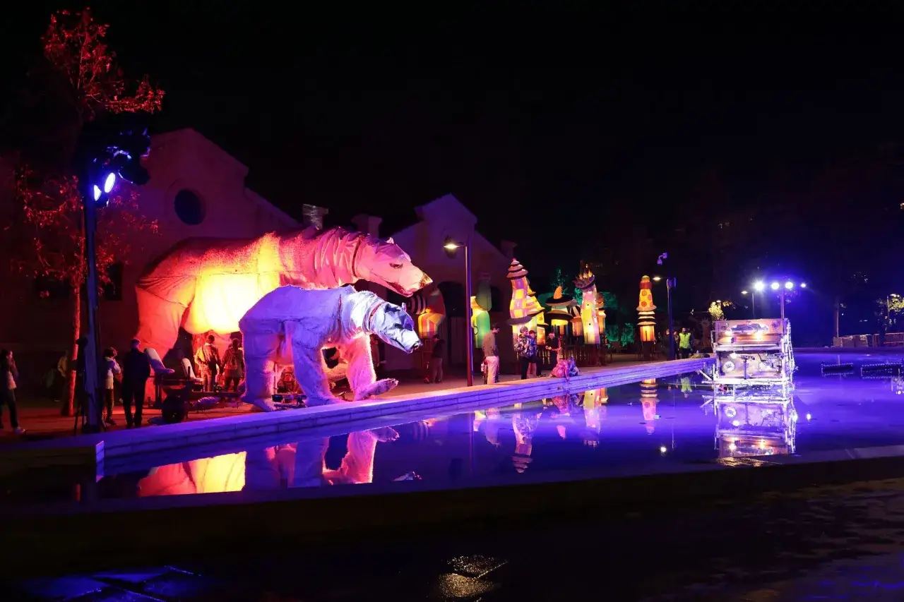 Gigantescos osos de peluche iluminados y coloridas estructuras decoran el parque central valencia navidad, reflejándose en el agua.