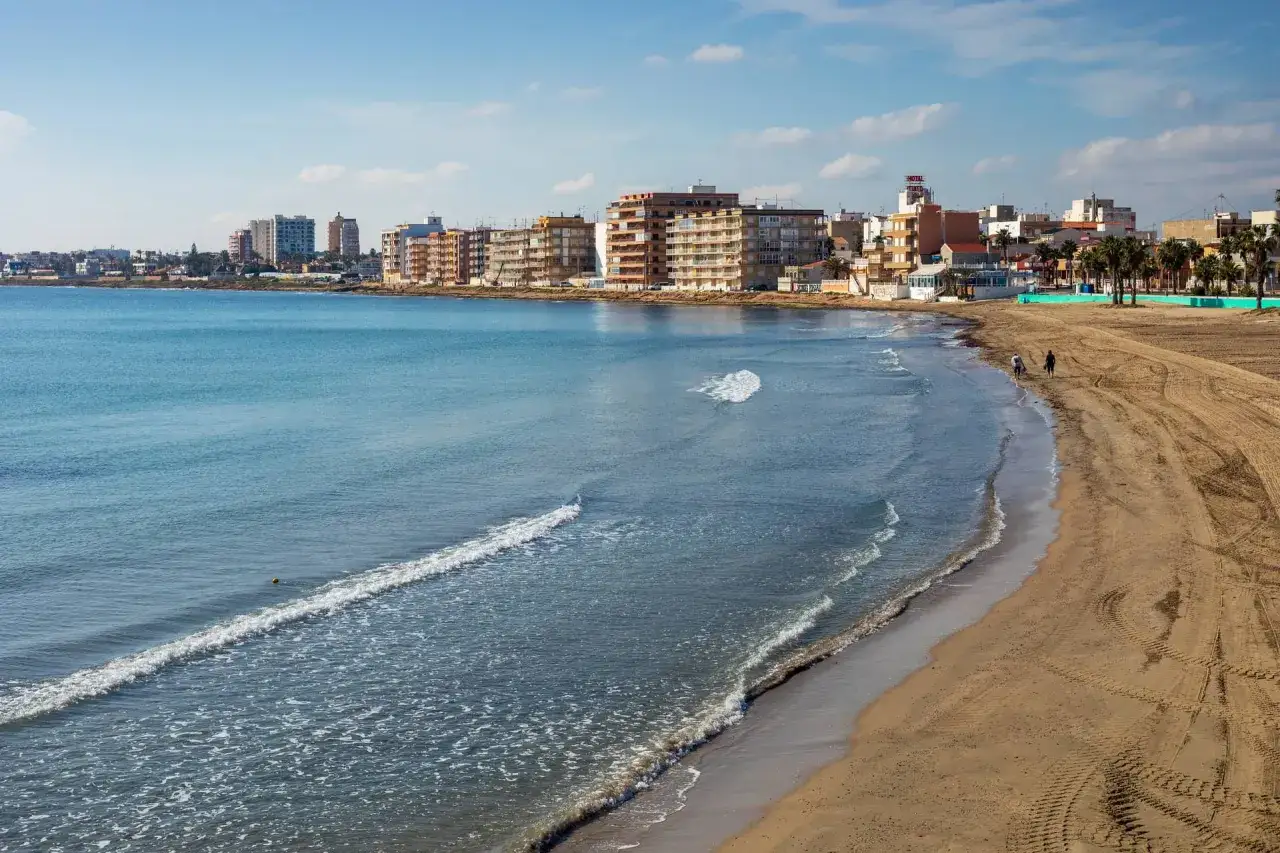 La playa de los naufragos, con edificios altos y palmeras, invita a pasear por su arena dorada mientras las olas acarician la costa.