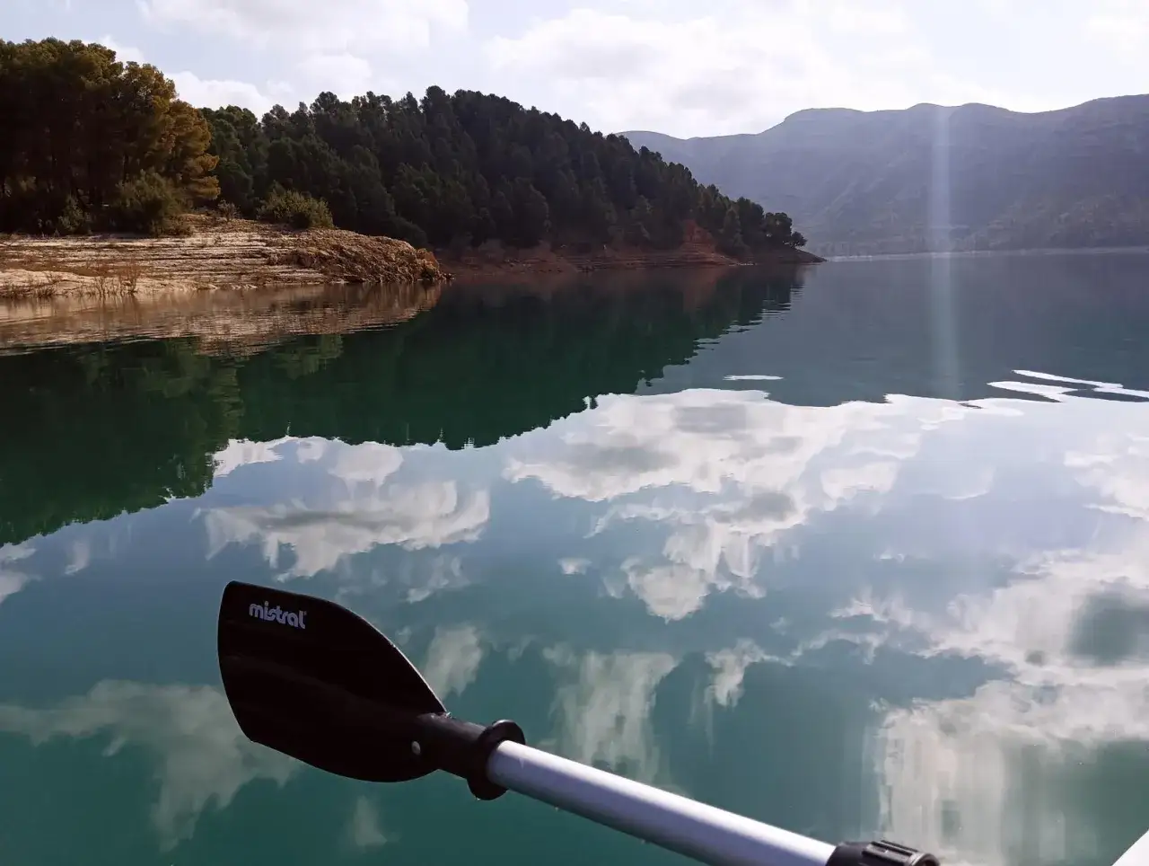 Remando en el embalse de Benagéber, con reflejos de nubes y montañas en el agua turquesa.
