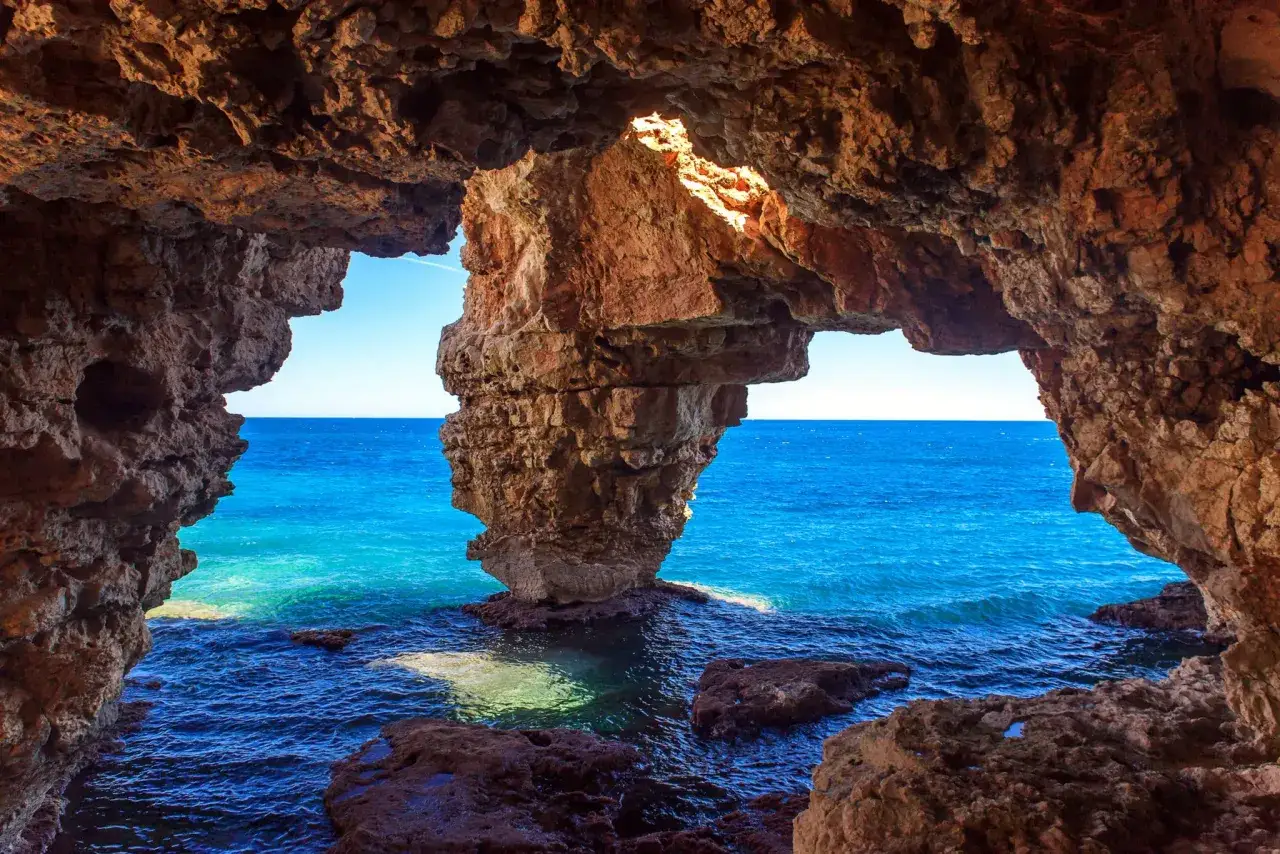 Vista desde una cueva en cala Moraig, con el mar azul intenso y formaciones rocosas.