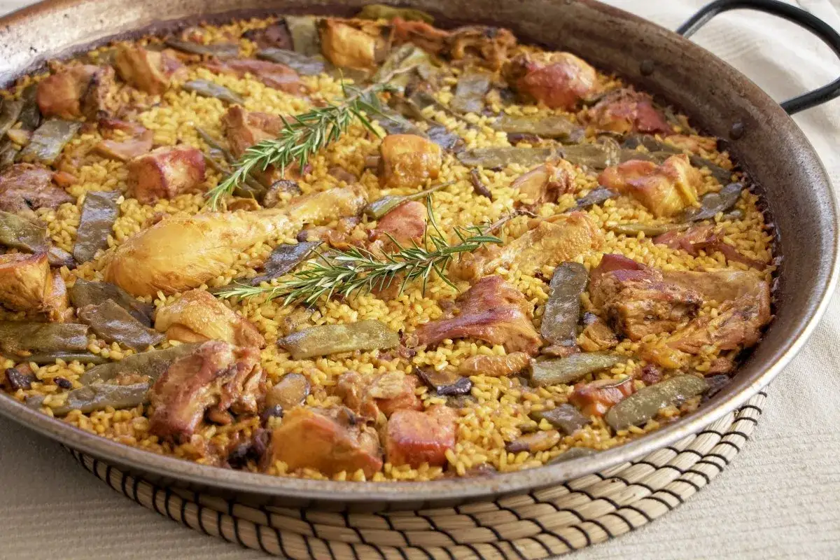 Paella valenciana recién hecha, con arroz amarillo, trozos de pollo, judías verdes y romero.