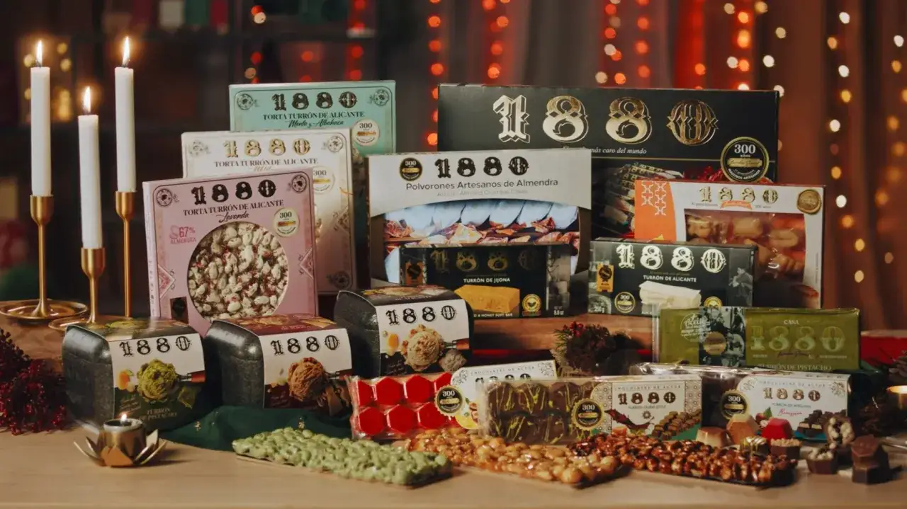 Una mesa llena de turrones 1880, velas encendidas y luces navide&ntilde;as. Variedad de turrones de almendra, pistacho y avellana.