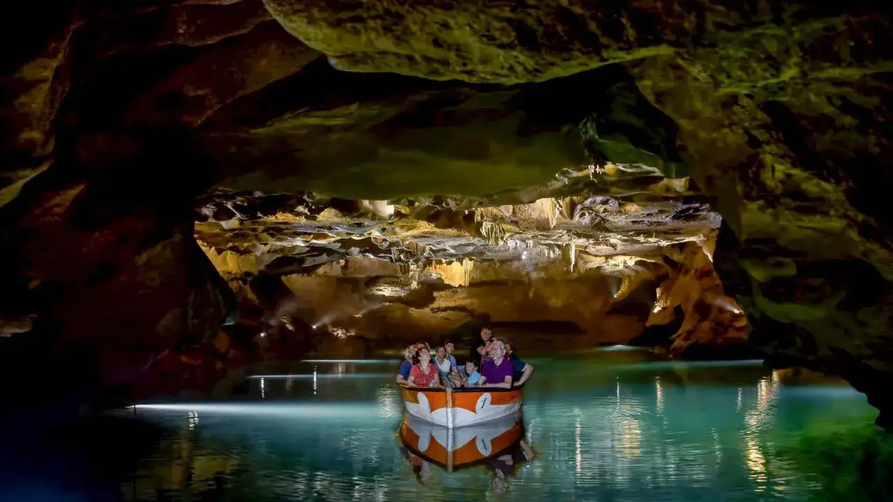 Barca con turistas navega por aguas turquesas en las cuevas de Vall d'Uixó. Consulta horarios y precios para tu visita.