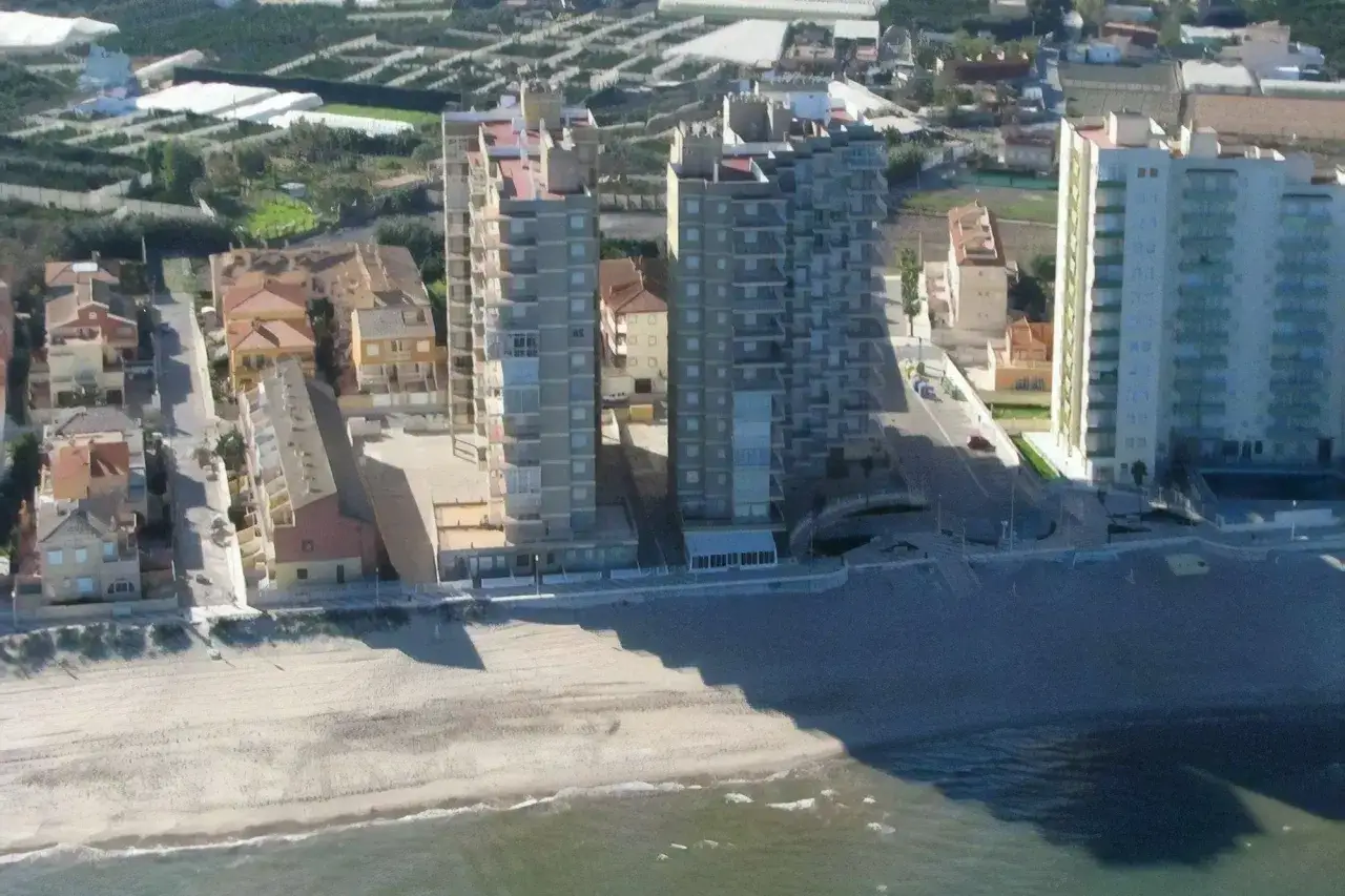 Edificios altos y casas bajas bordean la playa de Mareny de Barraquetes. El mar Mediterráneo acaricia la arena dorada.