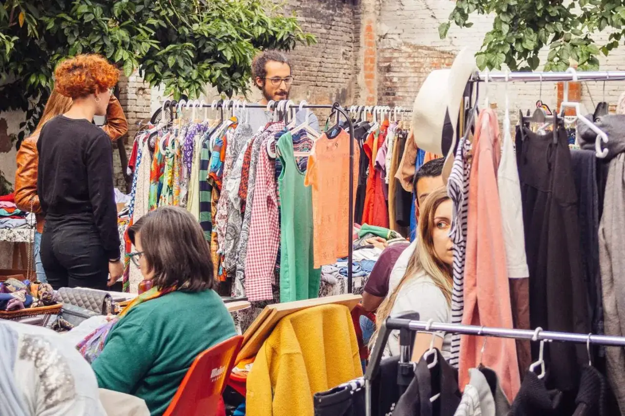 Gente buscando tesoros en el mercadillo Ruzafa. Ropa colorida y ambiente animado.