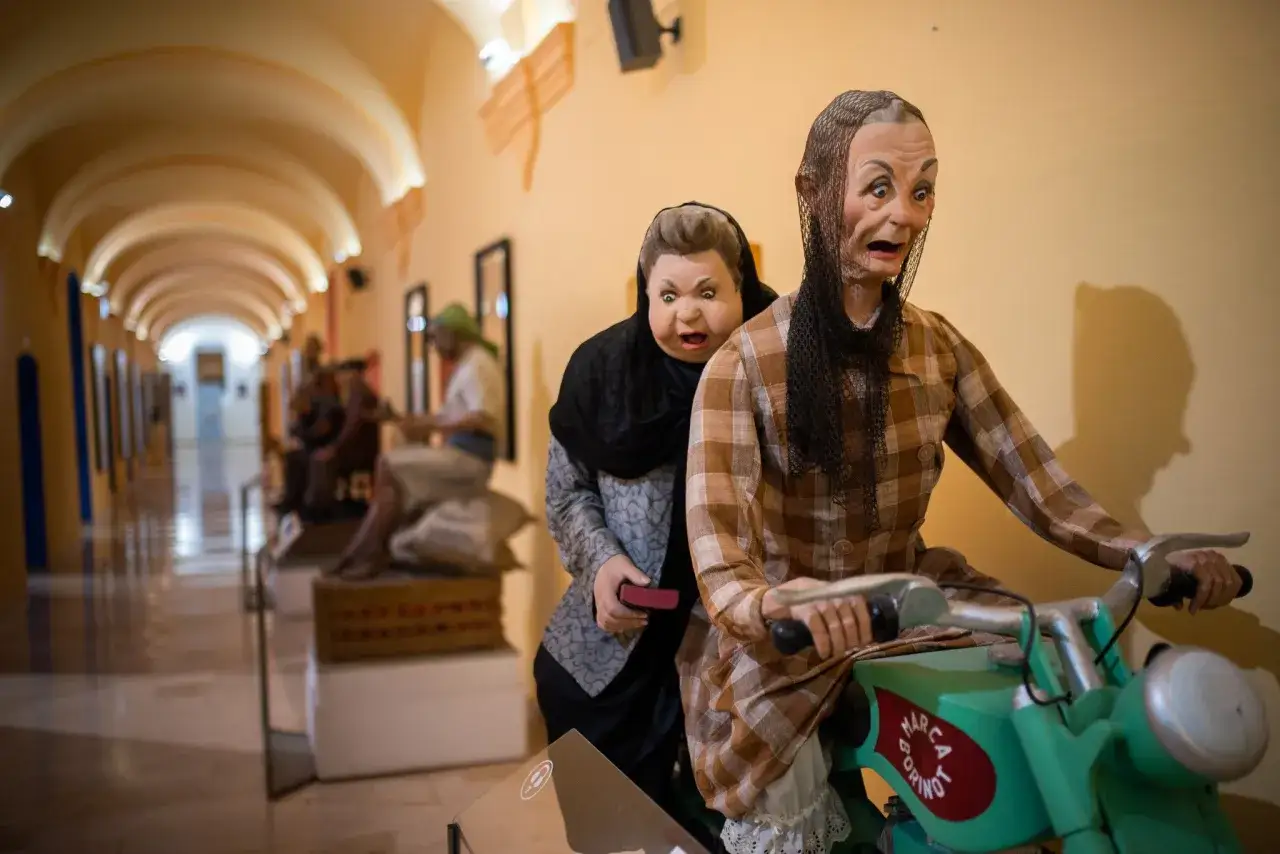Figuras realistas en un museo fallero recrean una escena c&oacute;mica de dos mujeres en una moto.