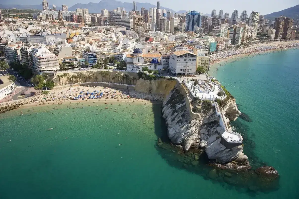 Vista aérea de la mejor playa de Benidorm, con gente disfrutando del sol y el mar turquesa, y la ciudad al fondo.