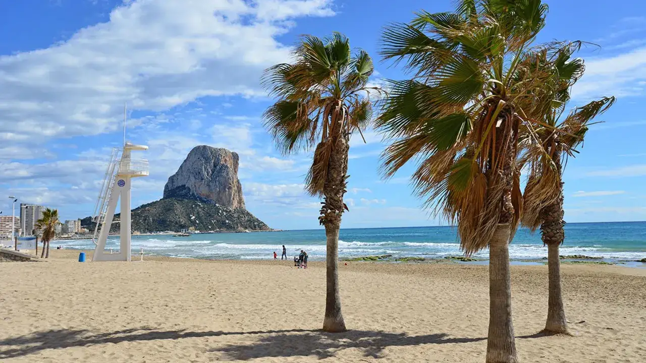 Palmeras en la playa del arenal-bol con un peñón al fondo y una torre de vigilancia.