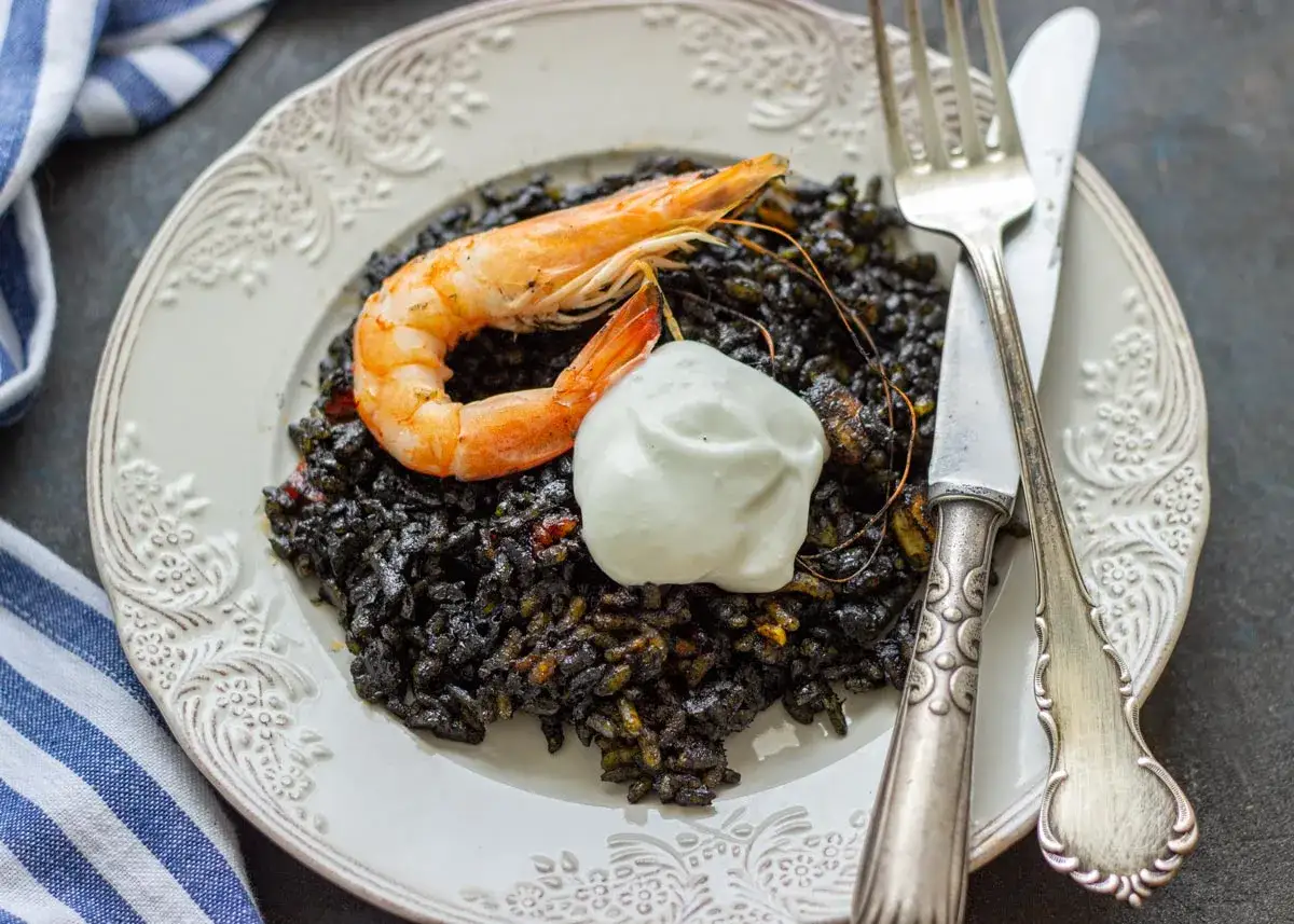 Un plato de arroz a banda negro, coronado con un langostino y una cucharada de alioli.