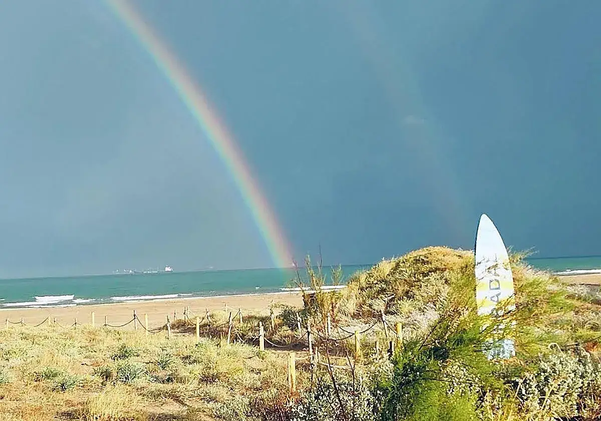 Arcoíris sobre la moncofar playa, con un tabla de surf blanca y azul en primer plano.