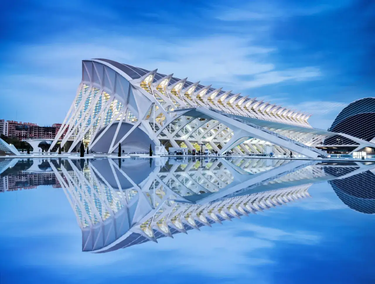 La Ciudad de las Artes y las Ciencias de Valencia, con su arquitectura futurista reflejada en el agua, bajo un cielo azul crepuscular.