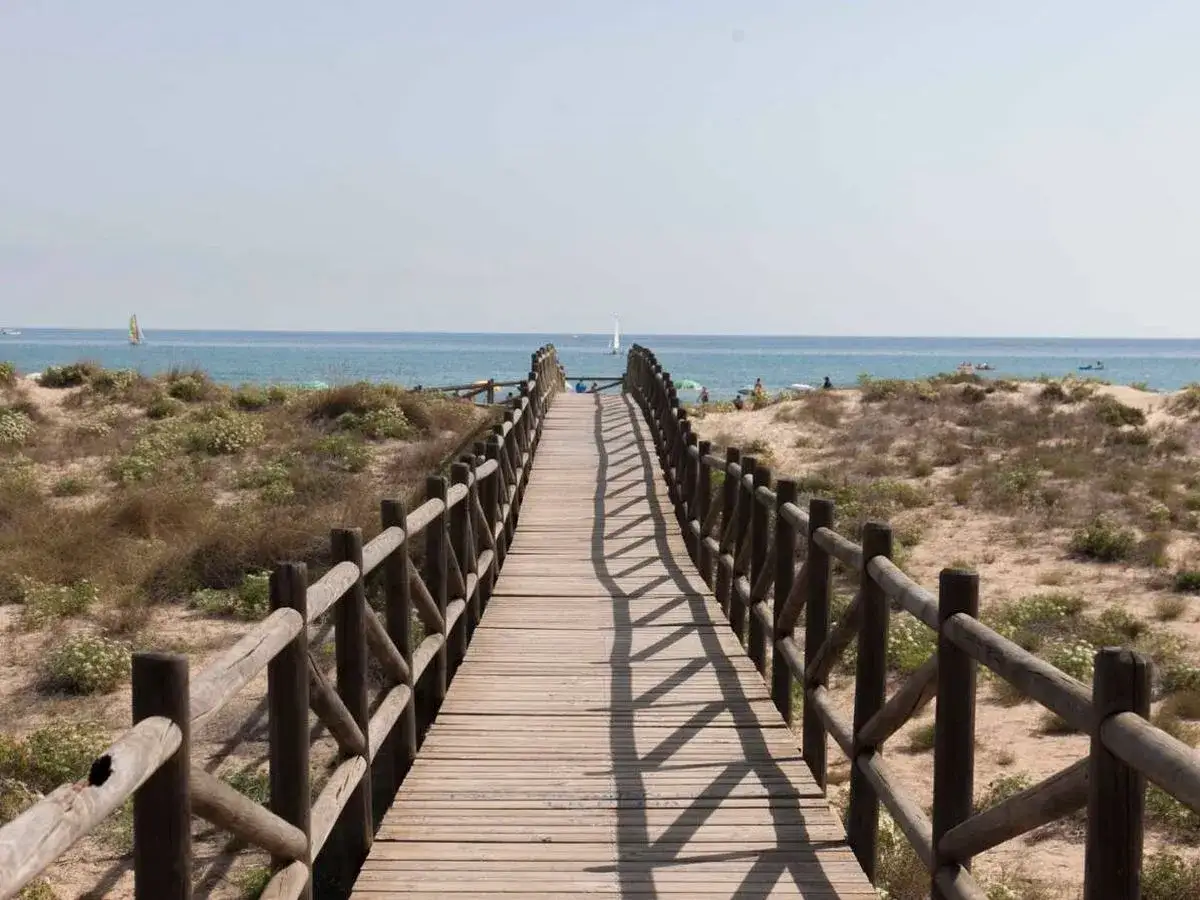 Pasarela de madera que conduce a la playa de Xeraco, con dunas y el mar azul al fondo.