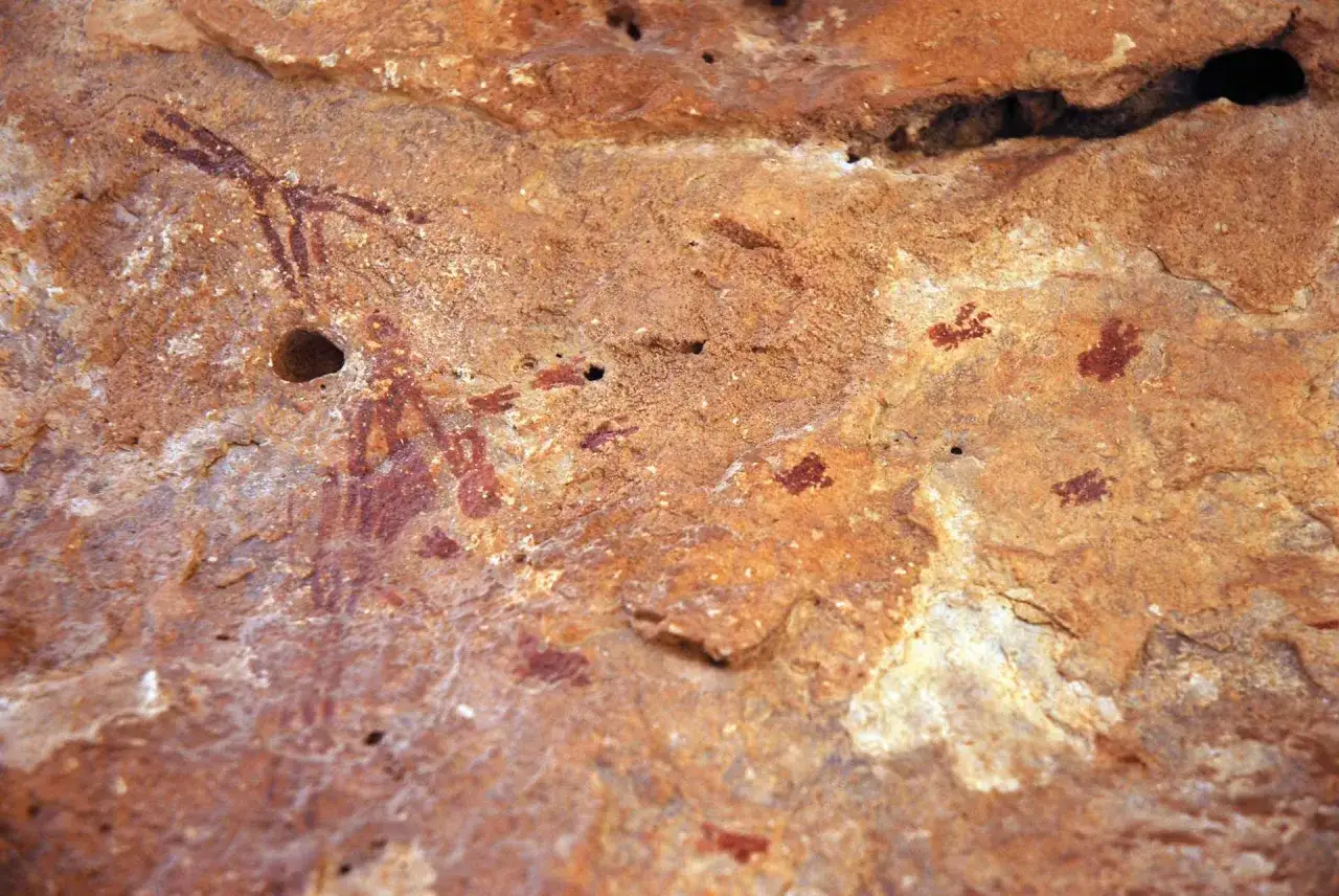 Pinturas rupestres en la cueva de la ara&ntilde;a: figuras antropomorfas y huellas de manos rojas sobre roca ocre.